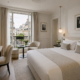 AI-generated chic white Paris hotel room with bed on the right, elegant mouldings, soft neutral decor, and realistic street view outside