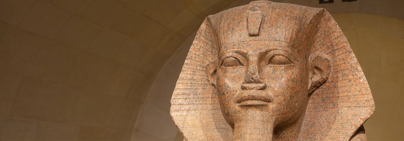 Colossal Egyptian Statue at the Louvre - Adobe Stock View of a colossal ancient Egyptian granite statue displayed in a vaulted gallery at the Louvre, showing the carved royal face and monumental scale of the sculpture.