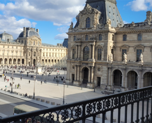 View of the Cour Napoléon at the Louvre. Source: Adobe Stock View of the Cour Napoléon at the Louvre in Paris, with the palace façades and part of the glass pyramid visible under a blue sky