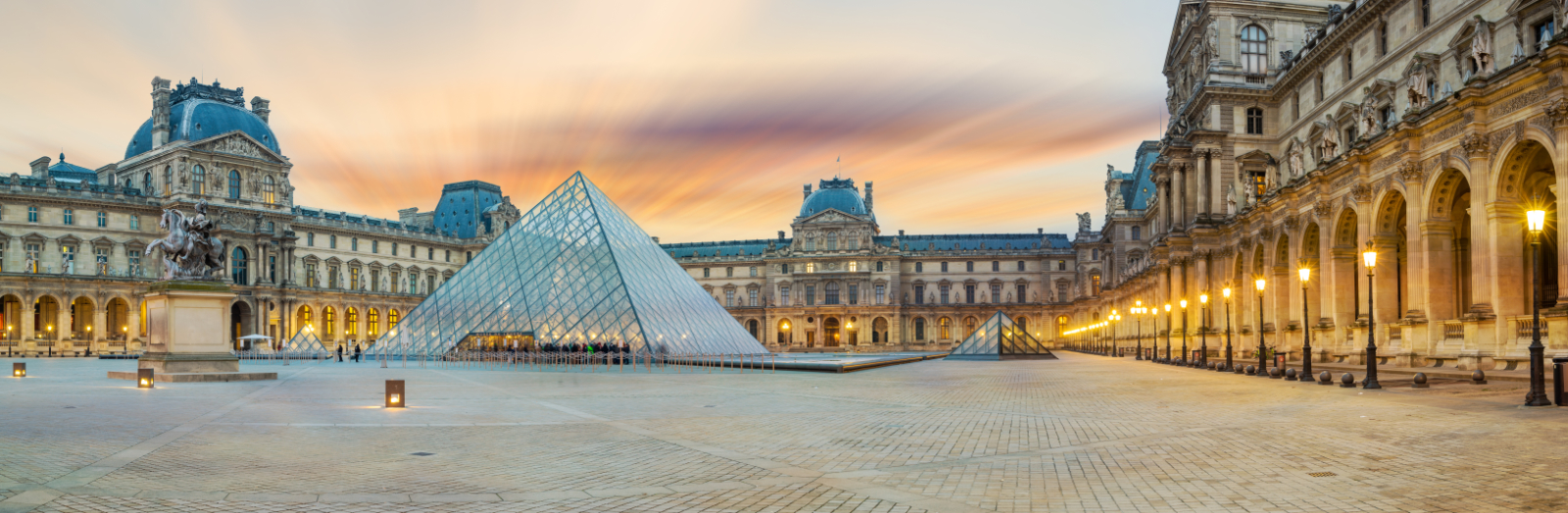 View of the Louvre Pyramid in the Cour Napoléon, with the surrounding palace façades and illuminated arcades at sunrise.