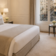 AI-generated luxury hotel room in Paris featuring a king bed, soft neutral tones, refined decor, balcony windows and classic city street view