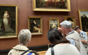 LOUVRE2004 Visitors examining Neoclassical French portraits in the Louvre Museum Denon wing — early 19th-century paintings by Ingres on a deep red gallery wall, visitors in conversation pointing at the works