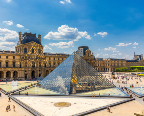 View of the Louvre Pyramid and Cour Napoléon. Source: Adobe Stock View of the Louvre Pyramid in Paris, with the surrounding palace façades and visitors crossing the Cour Napoléon under a bright blue sky