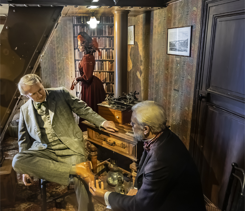 Adobe Stock view of the reconstructed Gustave Eiffel private apartment display inside the Eiffel Tower, with historical figures, a desk, wallpaper, bookshelves, and exposed metal structure