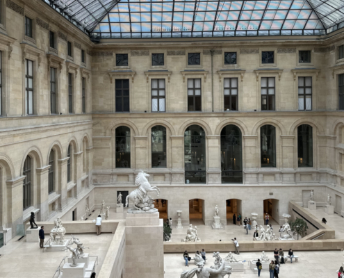View of the Cour Marly at the Louvre. View of the Cour Marly at the Louvre, showing the skylit sculpture courtyard with pale stone façades, monumental marble statues, and visitors moving through the open interior space.