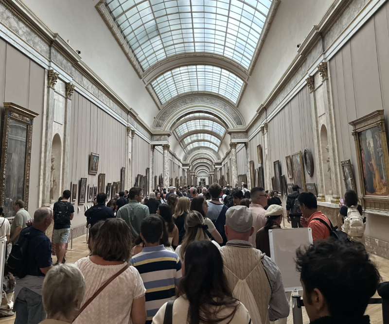 View of La Grande Galerie at the Louvre, showing the long skylit corridor lined with paintings and crowded with visitors moving through the gallery.