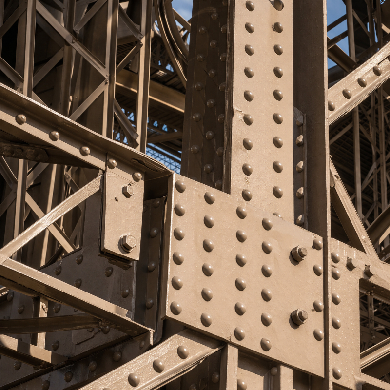 AI-generated square extreme close-up of the Eiffel Tower’s iron structure, showing rivets, bolted plates, intersecting beams, and precise metal joints in sharp architectural detail.