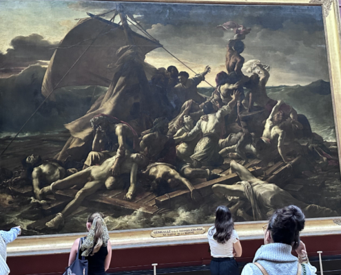 Adobe Stock view of The Raft of the Medusa at the Louvre. View of The Raft of the Medusa displayed at the Louvre, showing Géricault’s monumental shipwreck scene in a large gilded frame against deep red gallery walls, with visitors gathered in front of the painting.