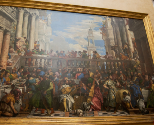 Adobe Stock view of The Wedding Feast at Cana at the Louvre. View of The Wedding Feast at Cana displayed in a large gilded frame at the Louvre, showing Veronese’s crowded banquet scene with Christ at the center beneath monumental Renaissance architecture.