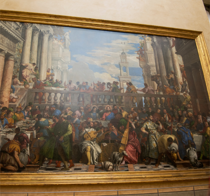View of The Wedding Feast at Cana displayed in a large gilded frame at the Louvre, showing Veronese’s crowded banquet scene with Christ at the center beneath monumental Renaissance architecture.