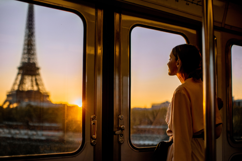 Woman enjoying morning view on the Eiffel tower View from inside a Paris metro carriage at sunset, showing a passenger looking out toward the Eiffel Tower through the train windows.
